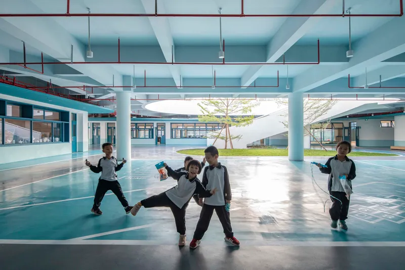 Covered courtyard with exposed blue-painted beams and columns where children play near a central tree