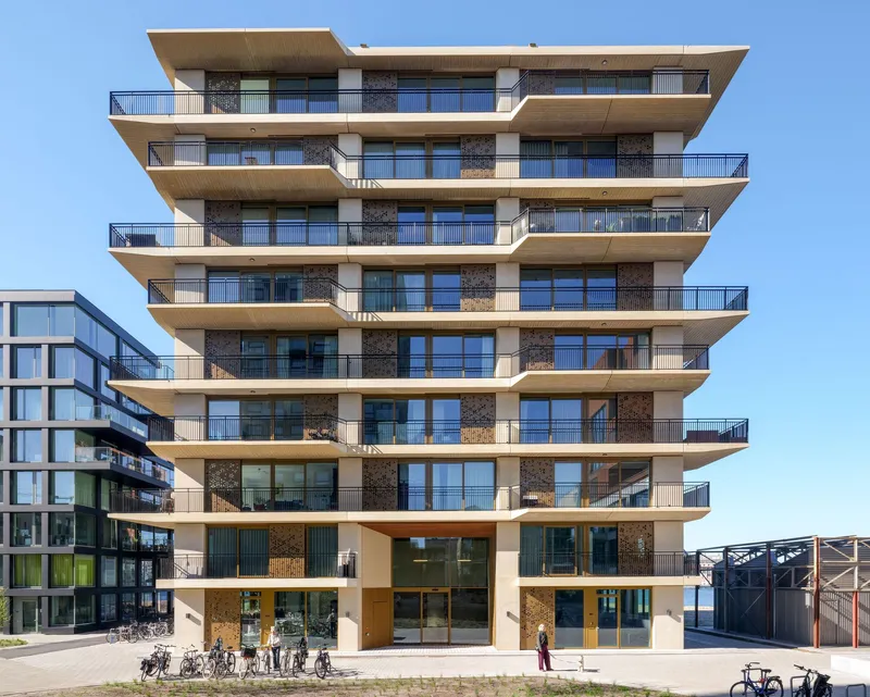 Stacked terrace facade with cantilevered floor slabs and bronze-clad balconies under clear blue sky