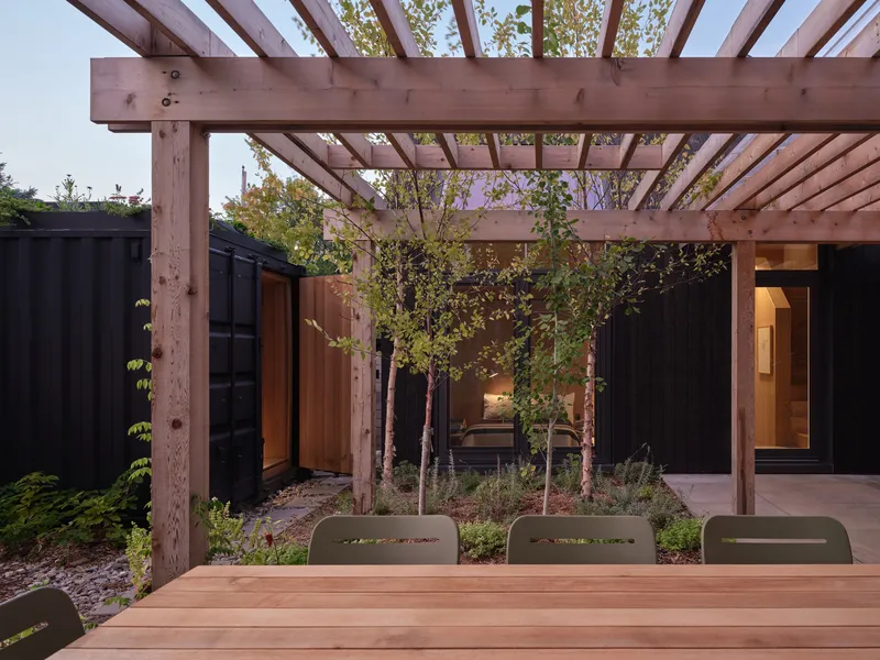 Timber pergola sheltering a courtyard with young trees and dark cladding at dusk