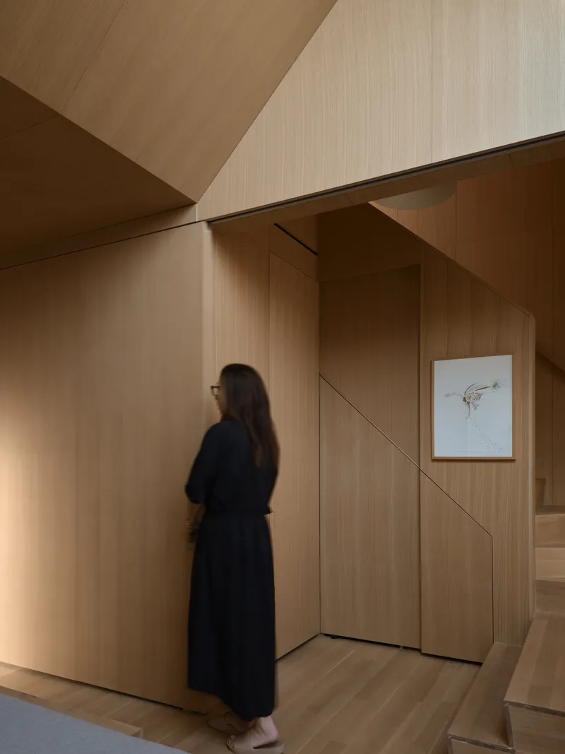 Person in dark clothing standing before a paneled wood wall with concealed doorways