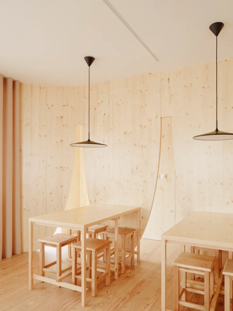 Dining tables with stools and pendant lights against pale plywood walls and vertical drapes