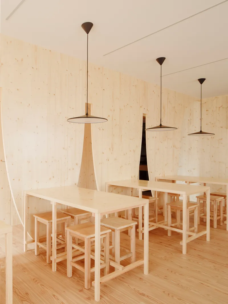Dining tables and stools arranged beneath three pendant lights and vertical sculptural forms