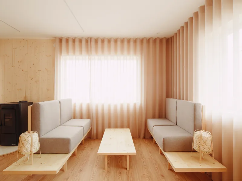 Corner seating area with upholstered benches and low table beneath pleated fabric curtains in warm light