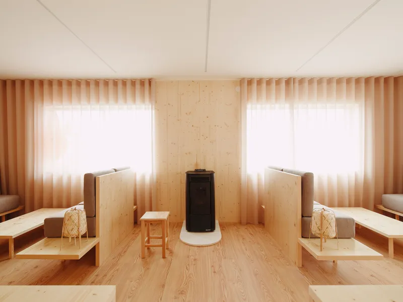 Central wood stove with white base flanked by windows with sheer curtains and timber privacy screens