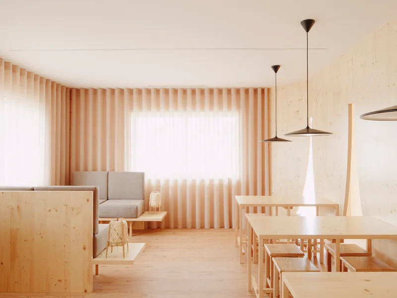 Light-filled dining area with pale timber furniture and vertical slatted curtains on corner windows
