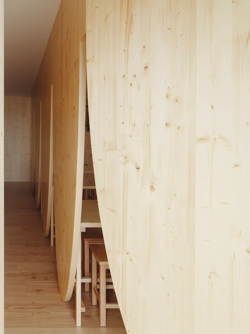 Glimpse through curved partition wall showing stacked stools and concrete in background