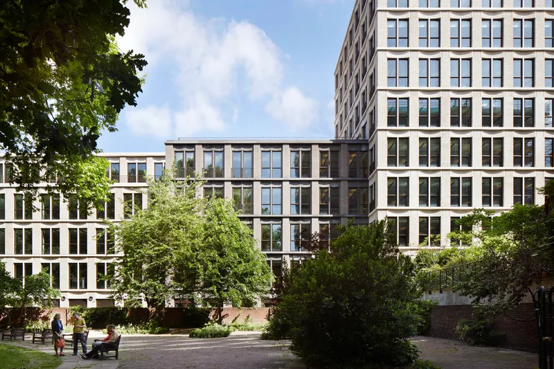 Courtyard view of the gridded window facades framed by mature trees and people on benches