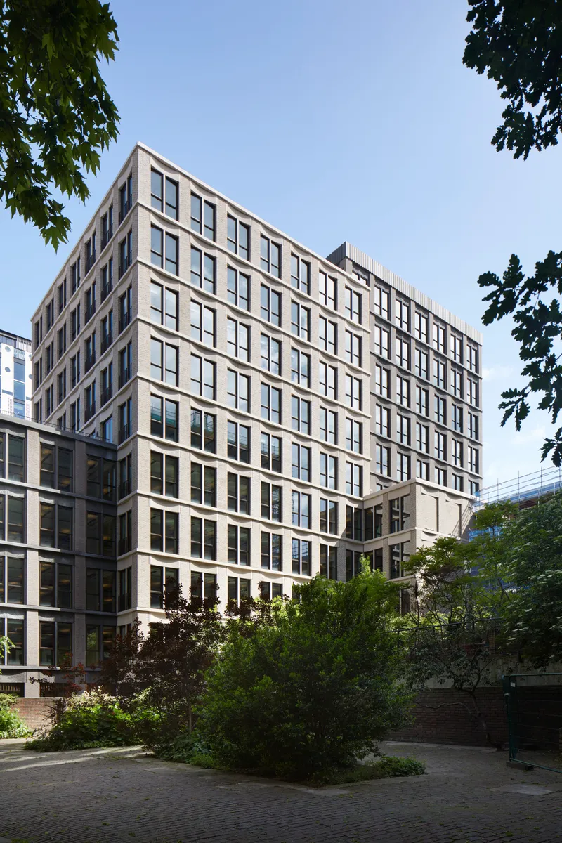 Multi-story facade with regular window grid and planted landscaping framed by tree canopy