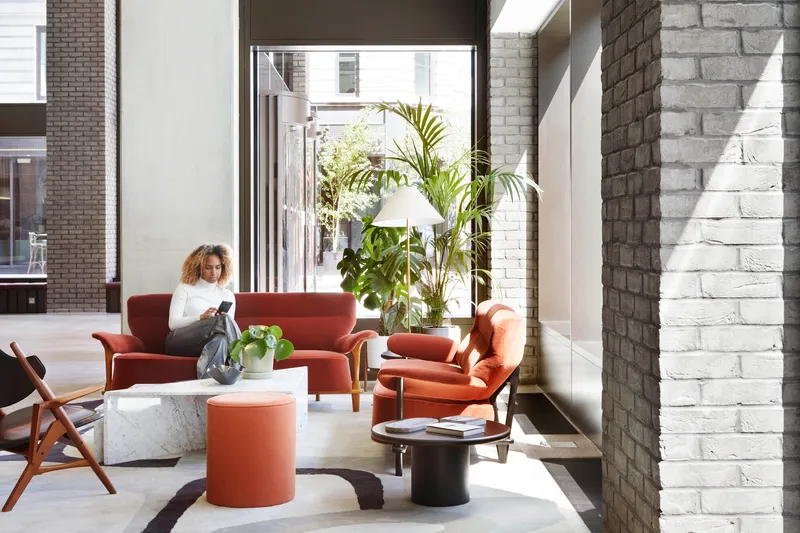 Ground floor lounge with terracotta upholstered seating, potted palms and white-painted brick walls
