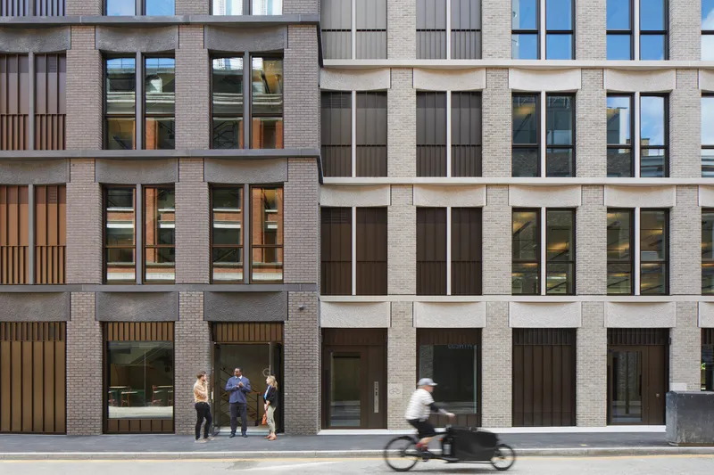 Street elevation showing mixed brick and stone facade with pedestrians and a cyclist passing by