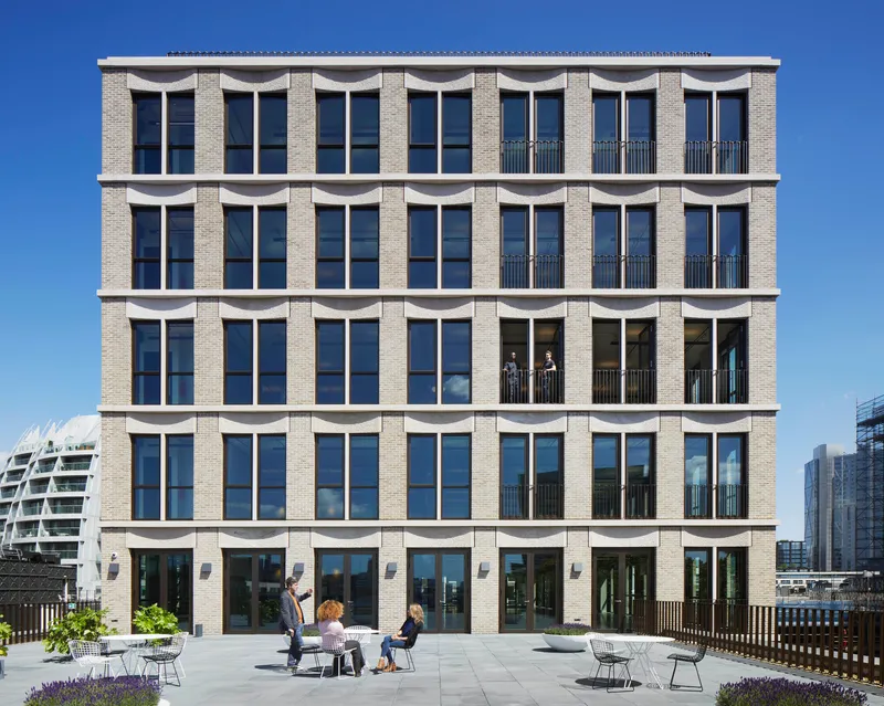 Five-storey brick facade with arched white concrete lintels and rooftop terrace with seated figures