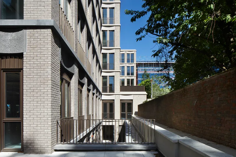 Courtyard view showing brick walls and metal railings framing a sunlit passage with tree foliage