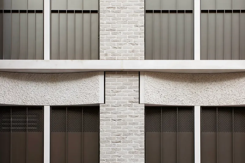 Facade detail showing white brick piers between grey metal panels and scalloped concrete spandrels