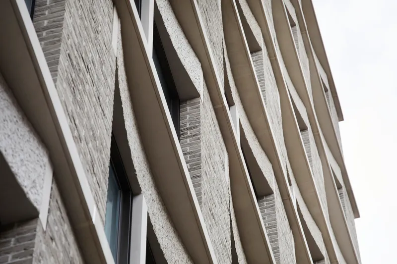 Angled view of the textured brick facade with projecting balcony fins under overcast skies
