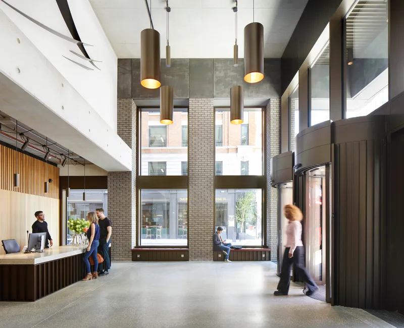 Double-height reception lobby with cylindrical bronze pendant lights and floor-to-ceiling windows overlooking the street