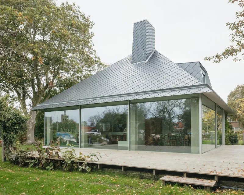 Glass-enclosed pavilion with sliding panels raised on a timber deck surrounded by lawn