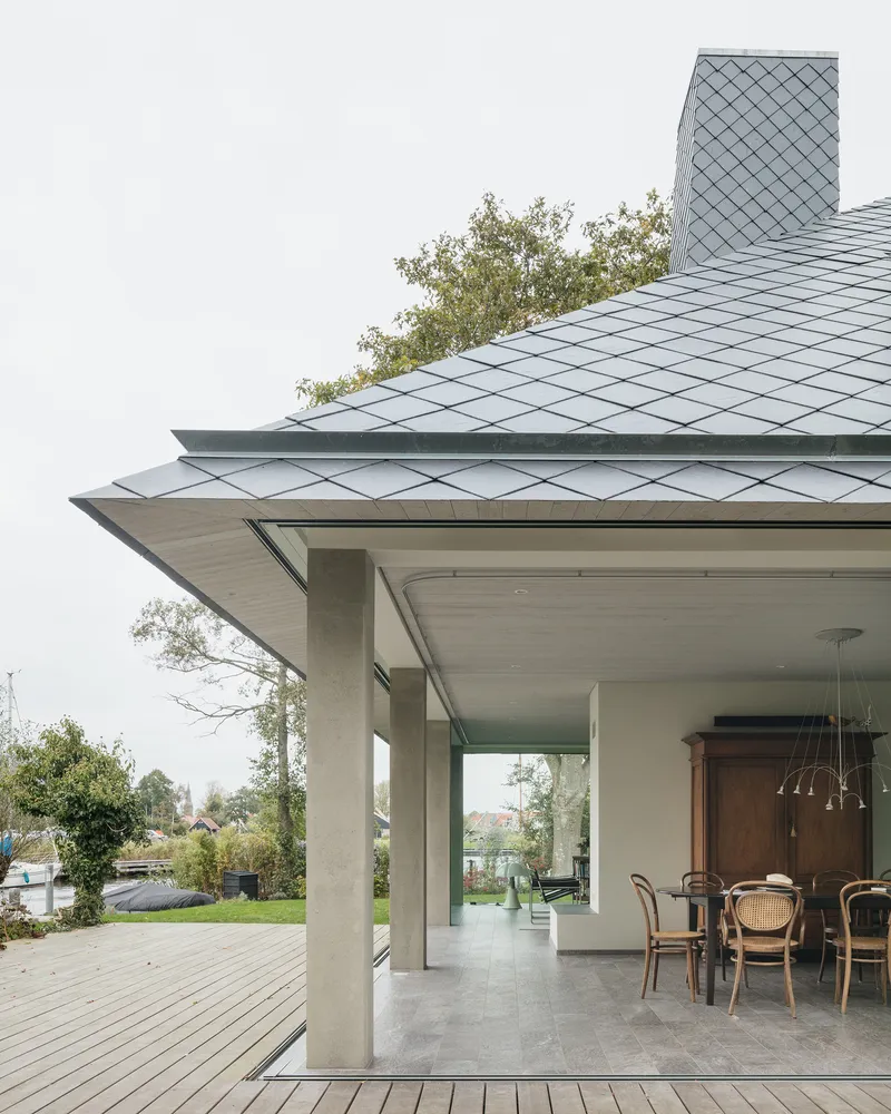 Detail of the overhanging roof eave with diamond-pattern zinc shingles above concrete columns