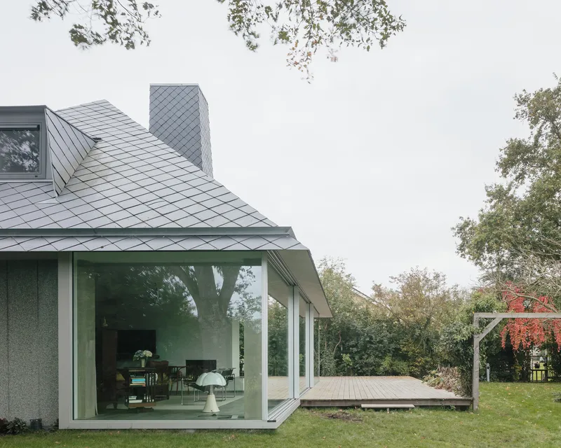 Garden facade with full-height glazing opening onto a timber deck under overcast skies