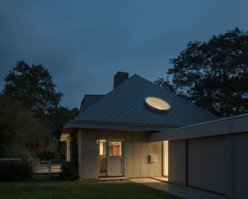 Entry facade with circular roof light above the glazed door at twilight