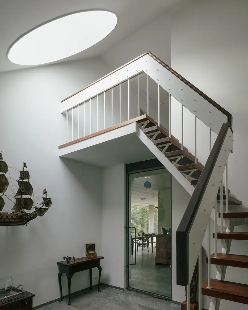 Interior staircase with timber treads and white vertical railings beneath an oval skylight