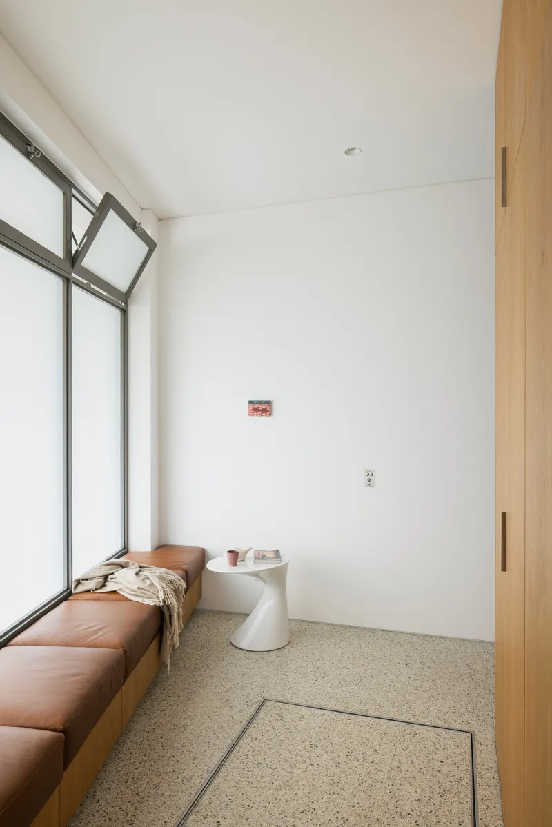 White-walled room with terrazzo flooring, steel-framed windows and a tan leather daybed