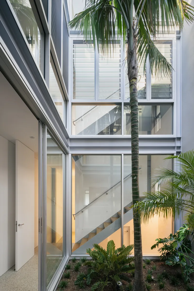 Interior courtyard view with palm tree and open staircase visible through glazed walls at twilight