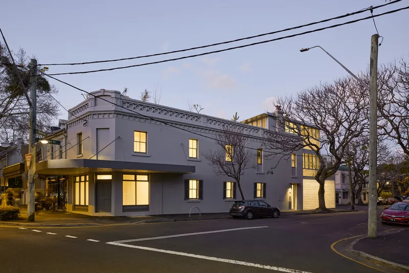 Corner facade with ornamental cornice and glass brick volumes glowing under overhead power lines at dusk