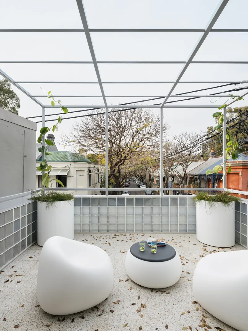 Outdoor courtyard with steel pergola overhead, glass block parapet and terrazzo floor scattered with leaves