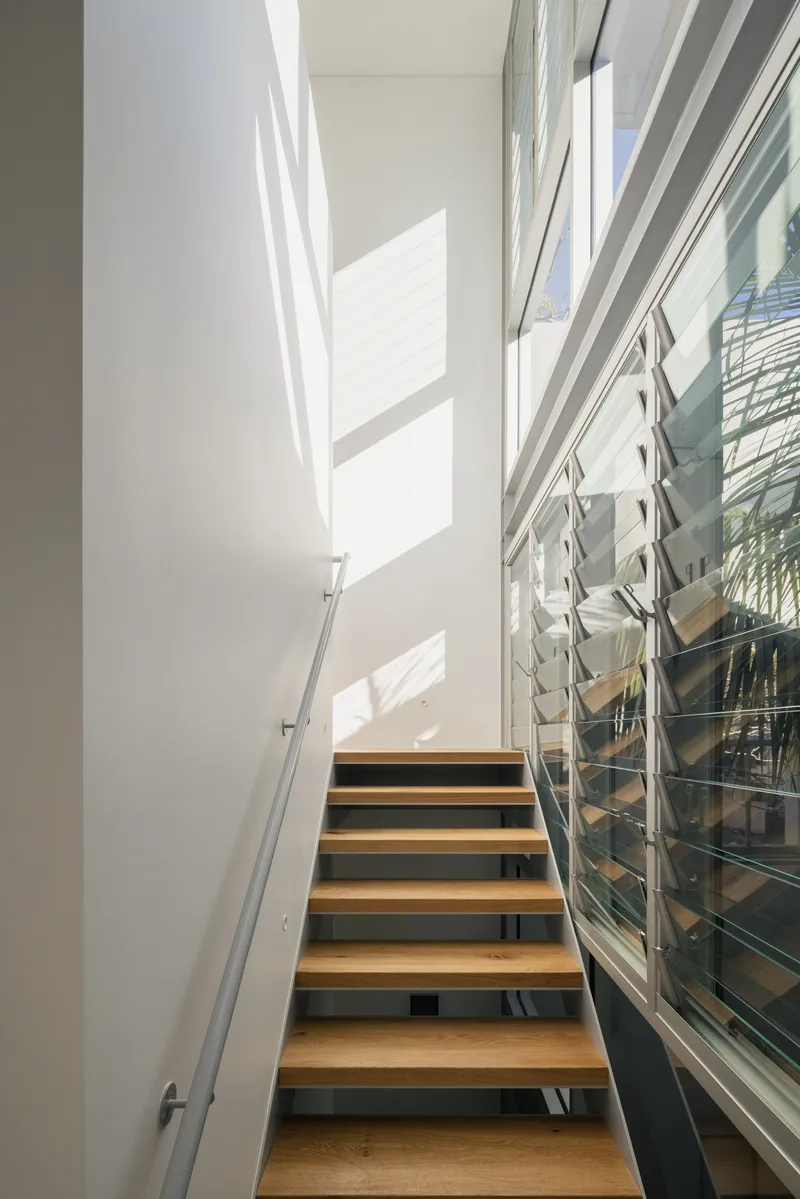 Timber-tread staircase with steel stringers alongside glazed louvered windows casting shadows