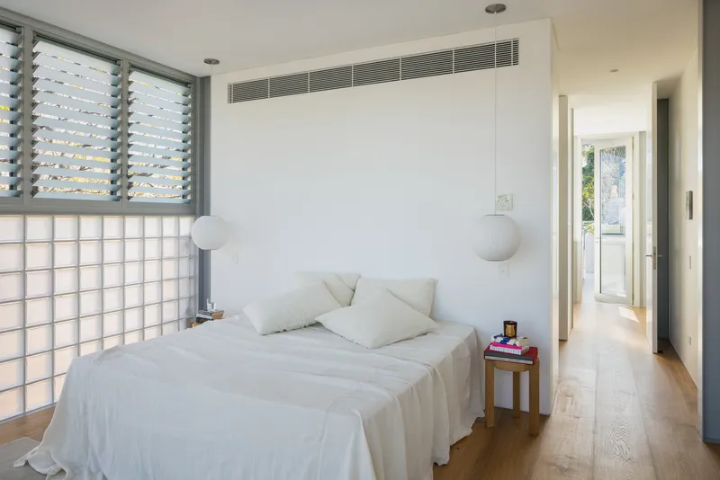 Bedroom with louvred window, glass block wall and recessed air conditioning grille above the bed