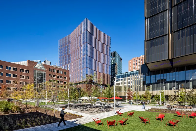 Public plaza with red lounge chairs on lawn and surrounding residential and office towers under blue sky