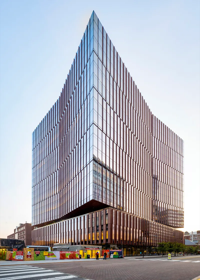 Corner view of the tower showing vertical metal fin facade and cantilevered podium above street level