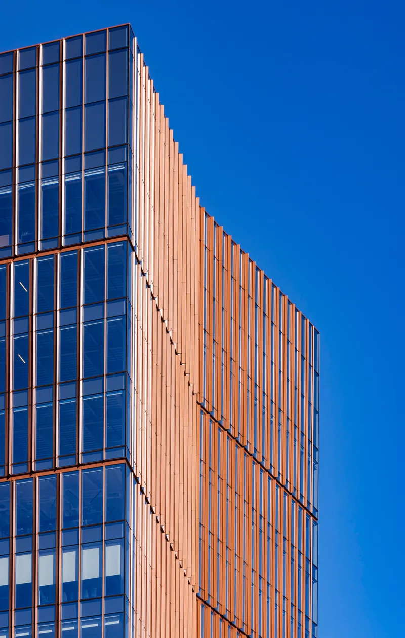 Close-up of the tower corner with bronze vertical fins against glass curtain wall and clear blue sky