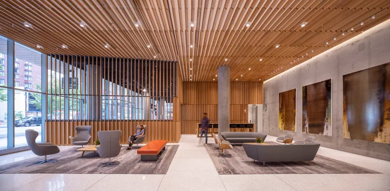 Double-height lobby with slatted wood ceiling, concrete walls and seating groups with two figures visible