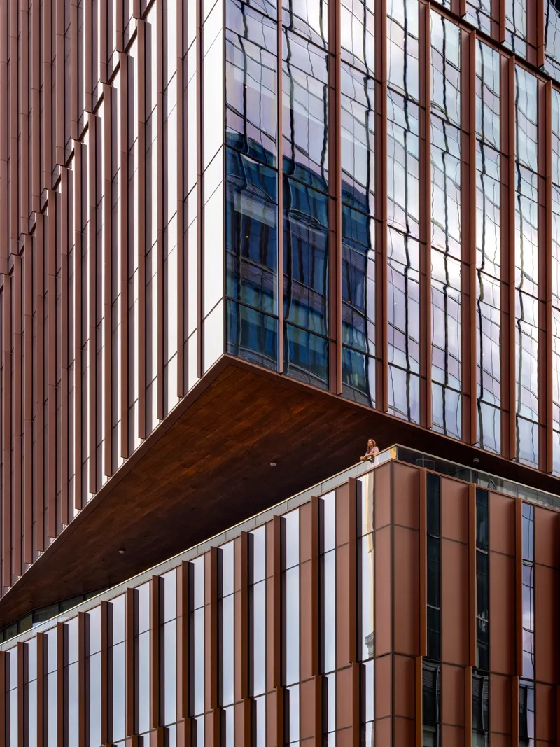 Close-up of the cantilevered volume with vertical bronze fins and glazed curtain wall above timber-clad lower floors
