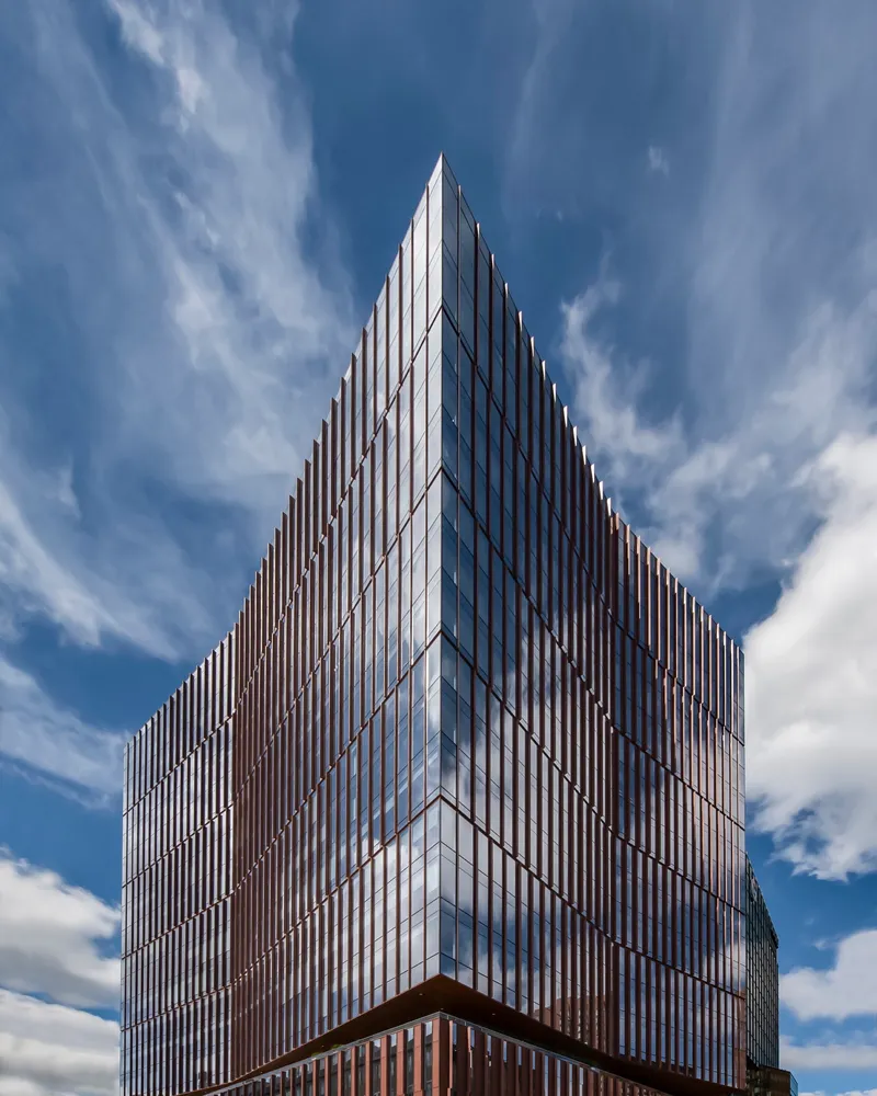 Tower facade with vertical bronze mullions and glazed curtain wall under a partly cloudy sky