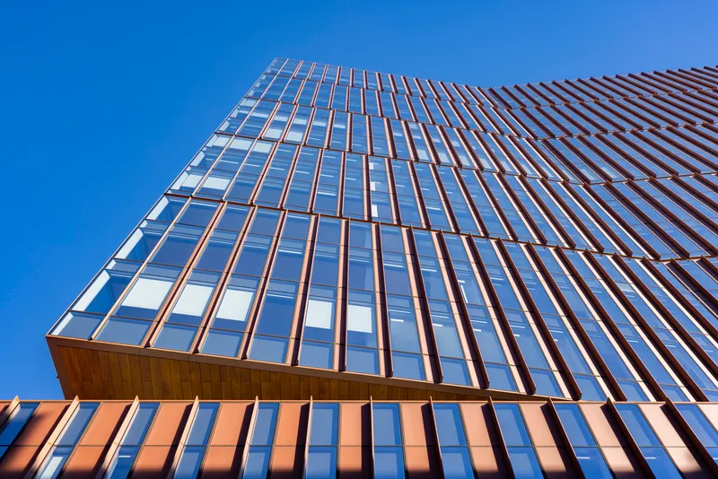 Upward view of the glazed tower facade with bronze vertical fins against a clear blue sky