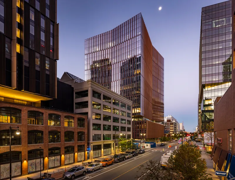 Street view of the tower rising above neighboring buildings at dusk with a crescent moon overhead