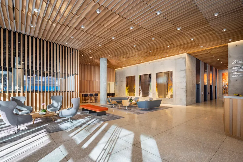 Lobby with slatted timber ceiling, concrete and marble walls, and sunlight patterns on the polished stone floor