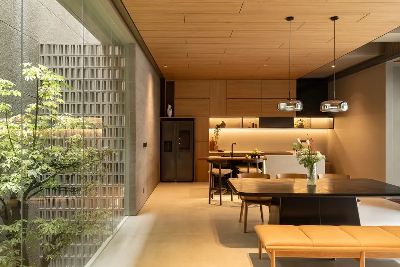 Open-plan dining and kitchen space with timber ceiling panels and a glass-enclosed courtyard planted with trees