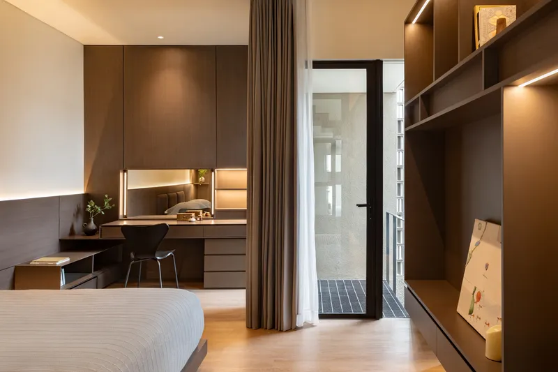 Bedroom with built-in desk and shelving leading to a narrow glass-brick lightwell beyond curtains