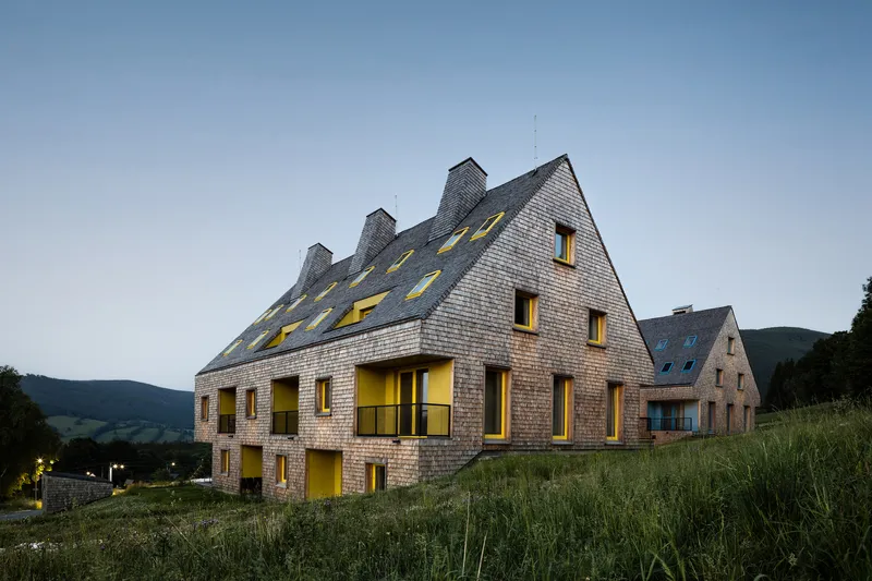 Shingled facade with yellow-framed windows and dormers illuminated at twilight on a hillside