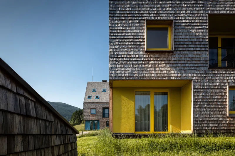 Yellow balcony projection with glass doors set into weathered timber shingle wall