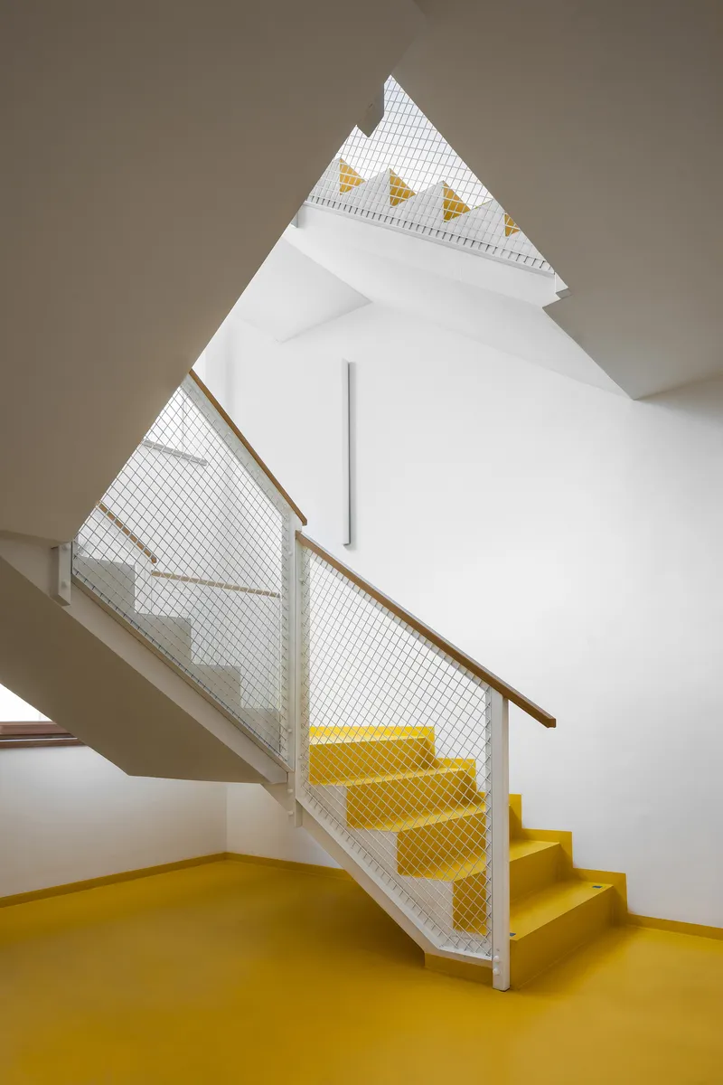 Interior staircase with yellow resin flooring and mesh balustrade beneath a skylit gable