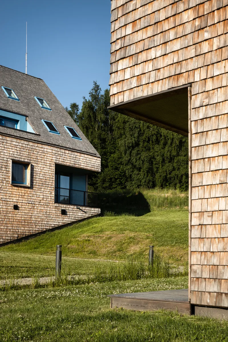 Cantilevered corner clad in timber shingles overlooking a mown lawn and adjacent gabled volumes