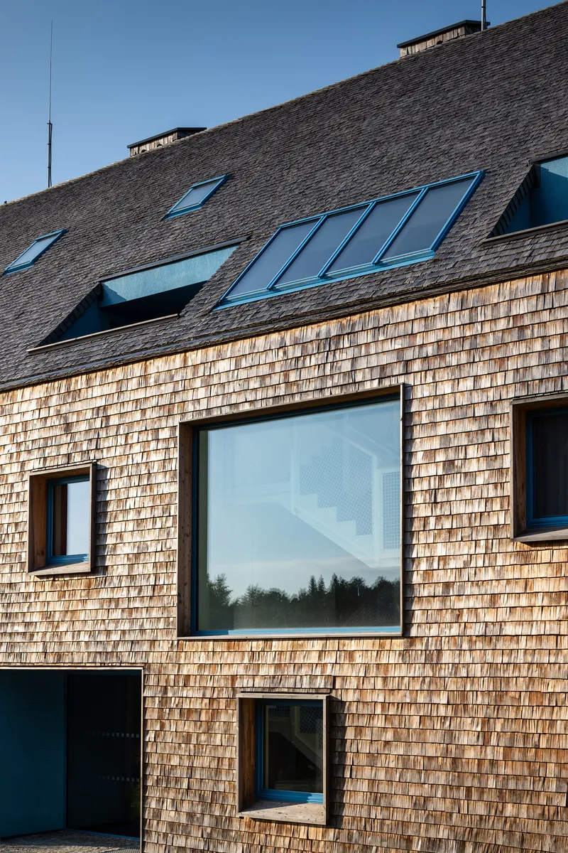 Timber shingle facade with varied window openings and skylights set into the pitched roof above