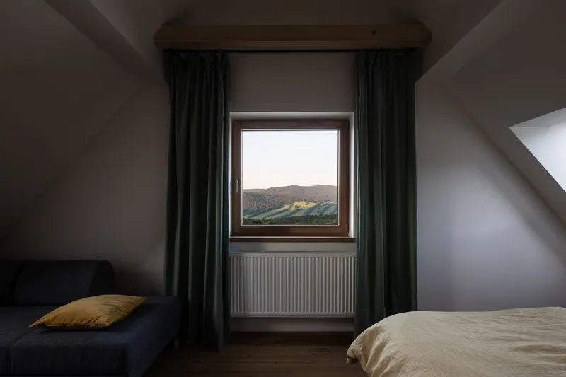 Bedroom window with dark curtains framing a view of the forested hills at dusk