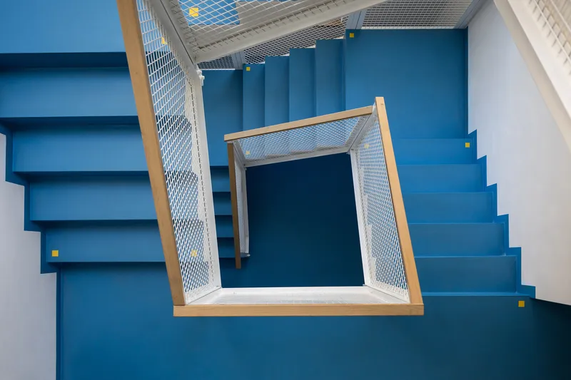 Top-down view of the stairwell with blue painted treads and timber-framed mesh balustrade