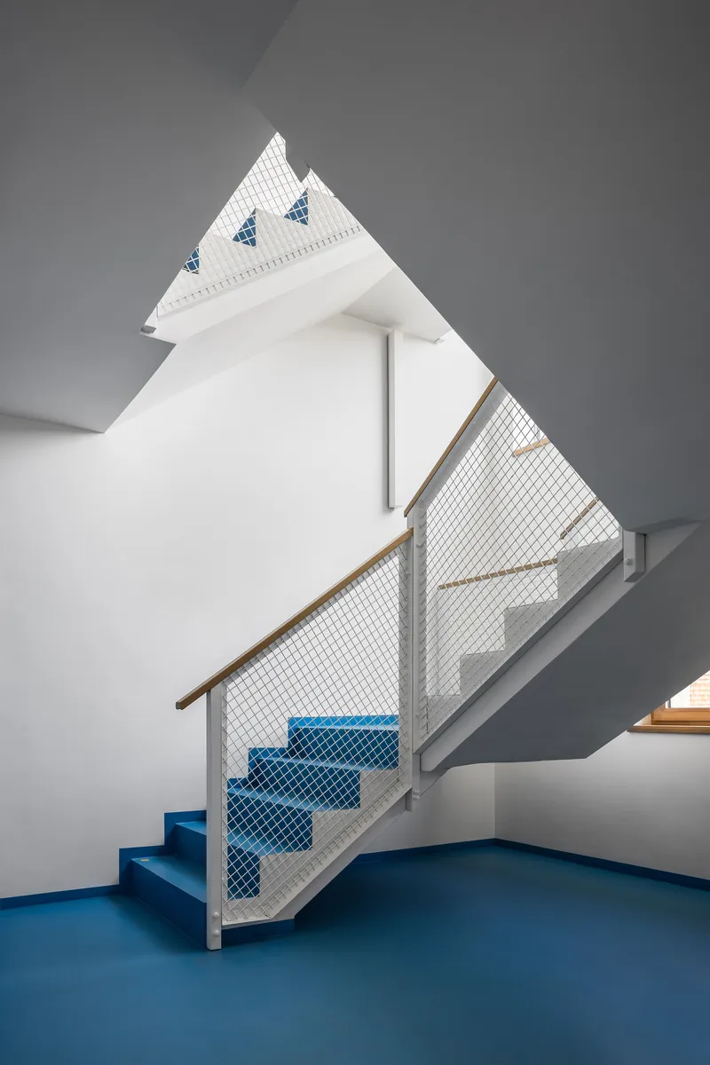 Interior staircase with blue treads and mesh infill under a peaked skylight