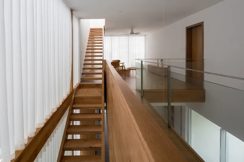 Timber staircase with open treads and glass balustrade alongside white vertical blinds in an upper corridor